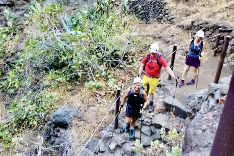 Wanderer steigen die felsige Masca Schlucht hinauf. Sie tragen Helme und Wanderstöcke.