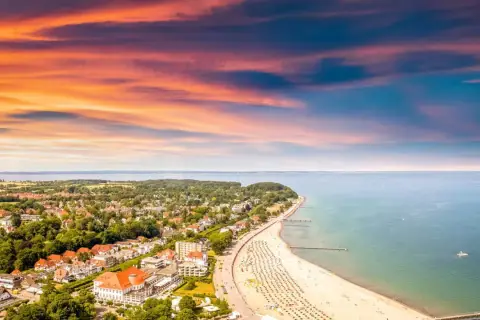 Ein perfekter tagesausflug ostsee: Sonnenuntergang über der Ostsee, belebter Strand mit Liegen und ein Küstenort mit roten Dächern.